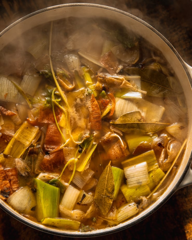 An overhead shot shows a pot of vegetable stock with the vegetables and herbs still intact in direct sunlight.