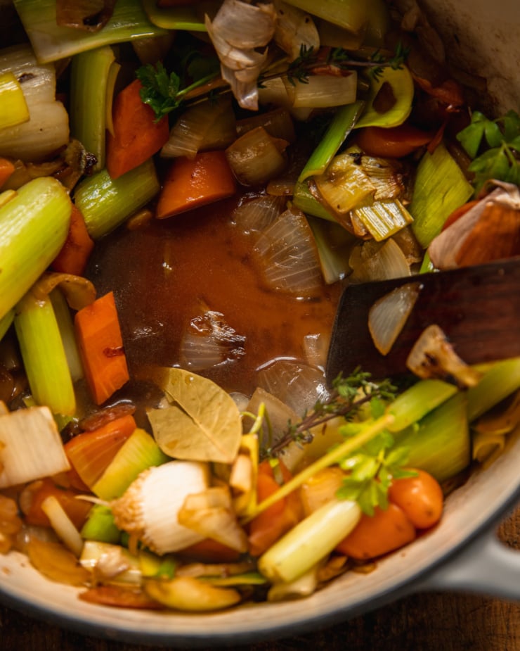 An overhead, up close shot, shows deep amber-coloured stock forming at the bottom of a pot of sautéed vegetables.