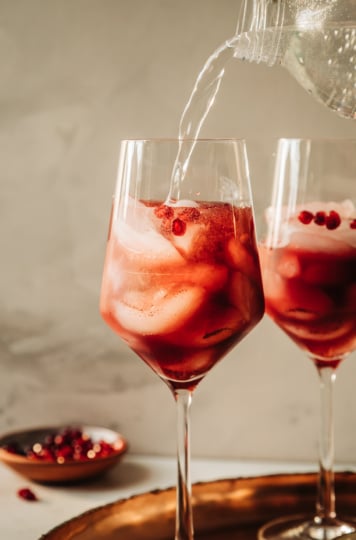 A head-on shot shows sparkling water topping off a pomegranate pomander spritz mocktail in a wine glass.