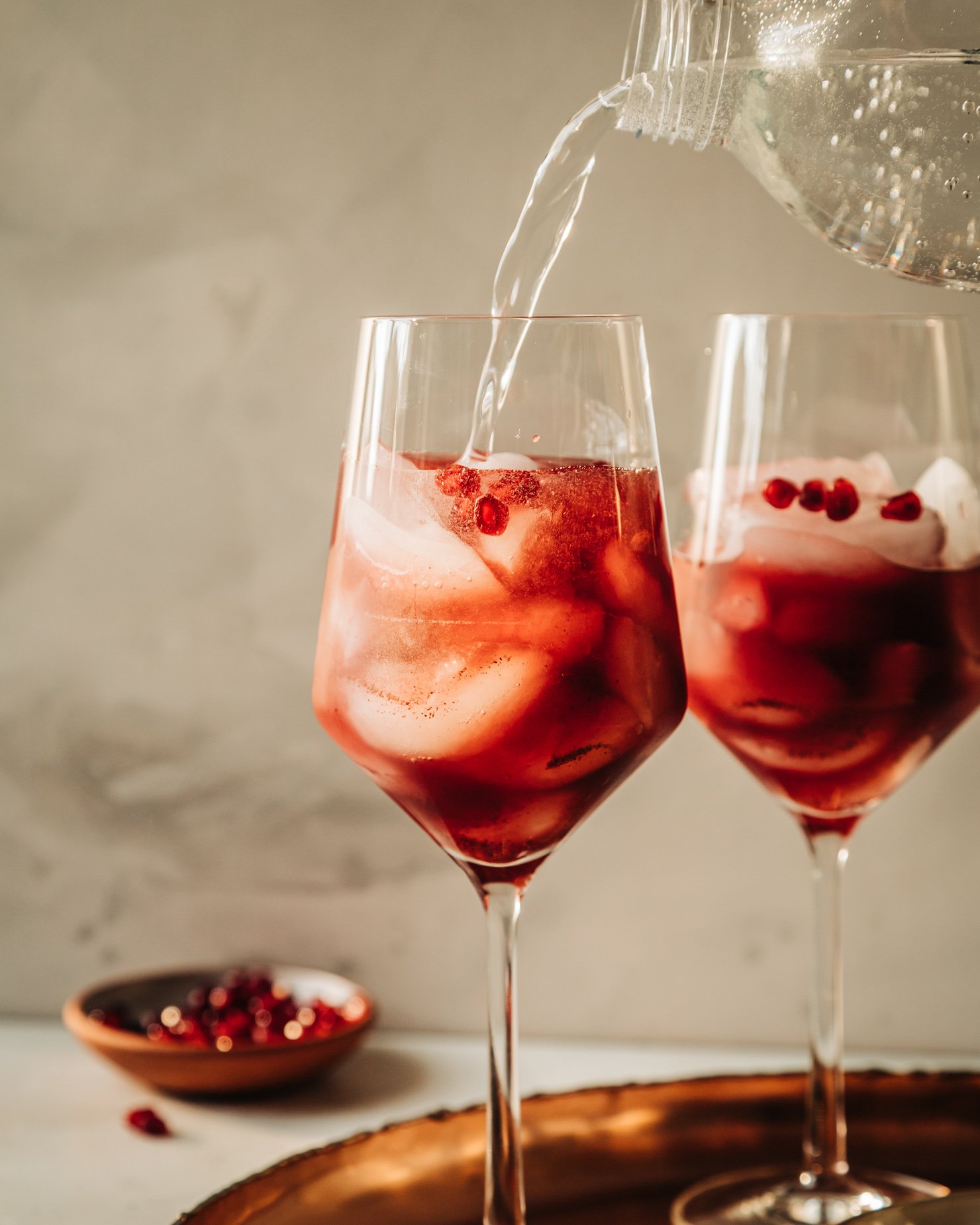 A head-on shot shows sparkling water topping off a pomegranate pomander spritz mocktail in a wine glass.