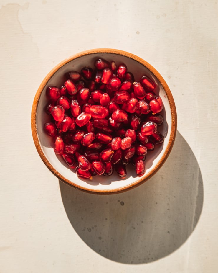 An overhead shot of some pomegranate arils in a small bowl in direct sunlight.