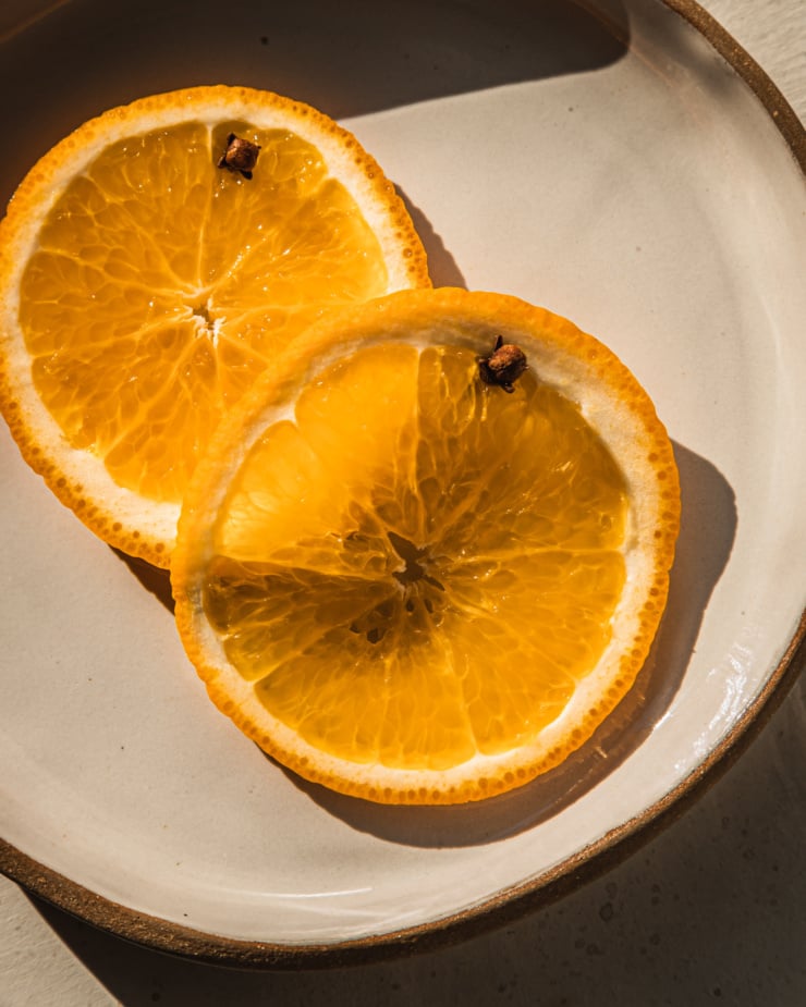 An up close, overhead shot of two orange slices with whole cloves stuck into them.