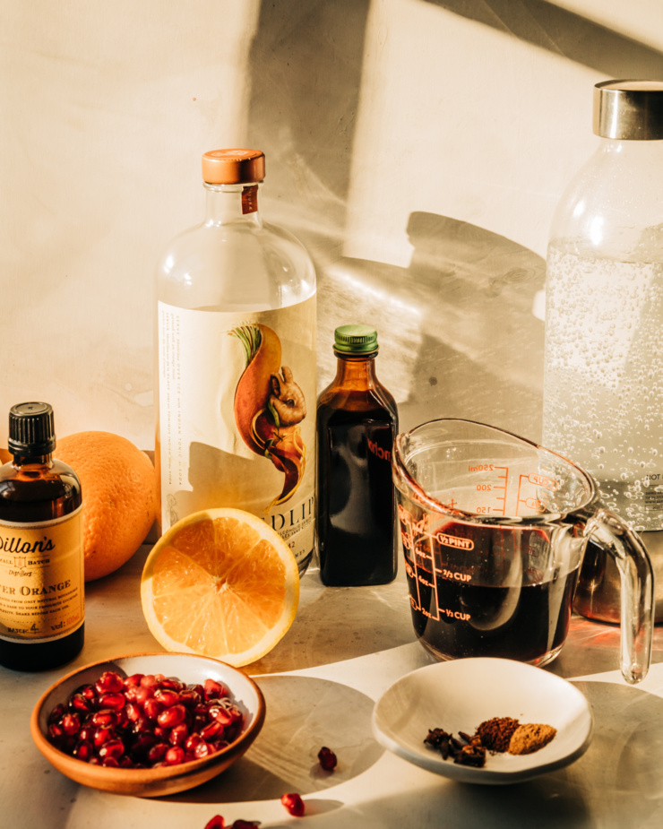 A head on shot of ingredients used to make a festive winter mocktail. All ingredients are shown against a white background in harsh direct light.