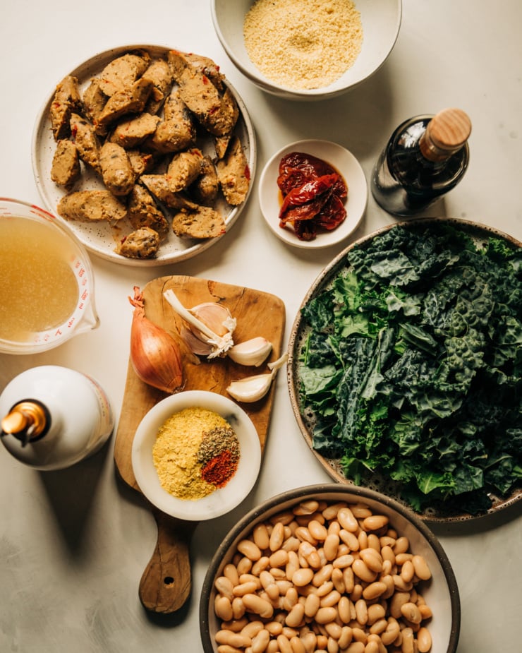An overhead shot of ingredients used in a veggie sausage white bean skillet against a white background.