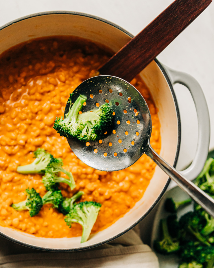 An overhead image shows broccoli being spooned on top of a creamy barley and white bean base.