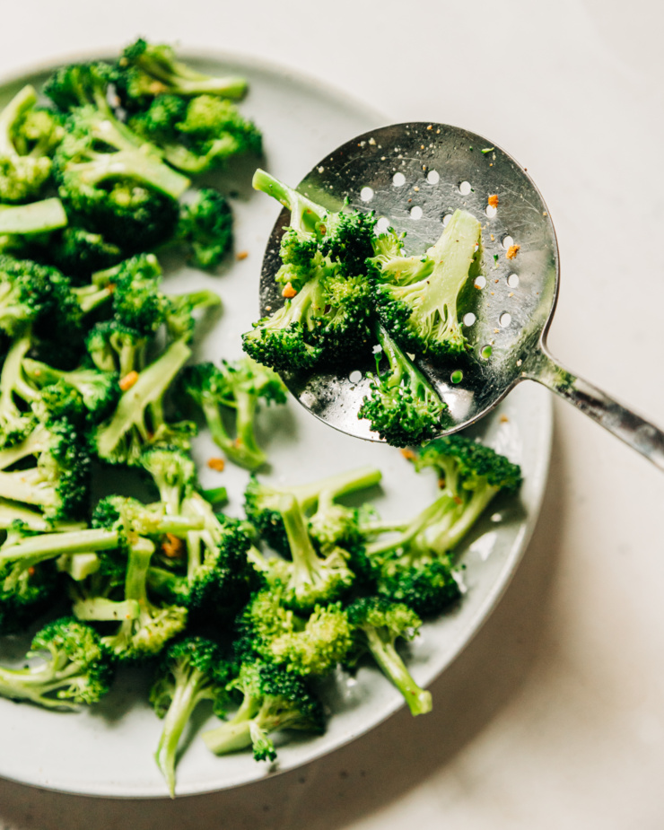 An overhead shot of sautรฉed broccoli being spooned onto a plate.