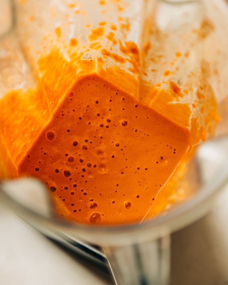 An overhead shot of a "cheesy" vegan red pepper and cashew sauce inside of a blender pitcher.