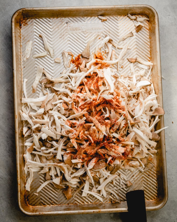 An overhead shot shows raw, shredded oyster mushrooms on a baking sheet, topped with paprika, garlic, and onion powders.