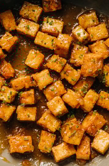 An up close, overhead shot shows sticky marmalade tofu in a non-stick skillet. The tofu cubes are swimming in a bit of the marmalade glaze and is garnished with chopped chives.
