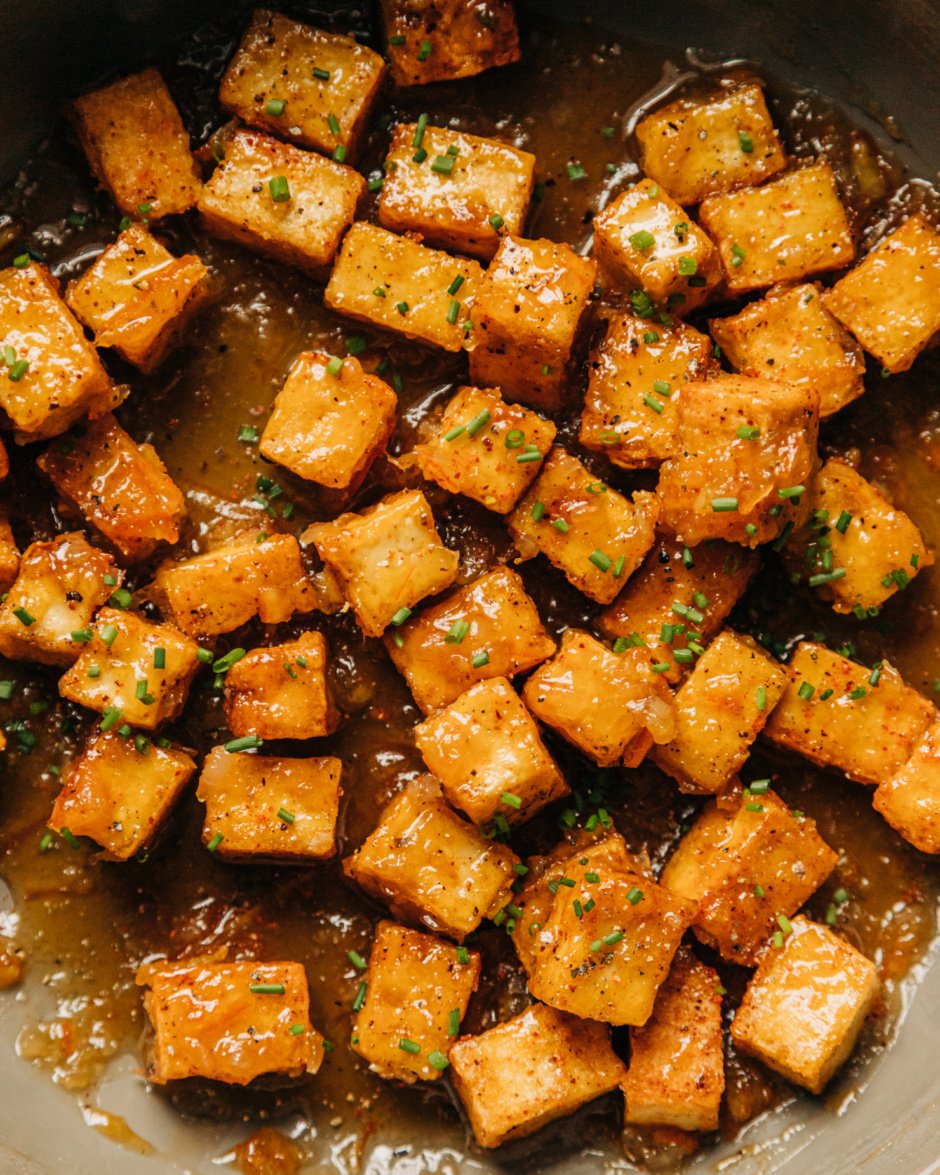 An up close, overhead shot shows sticky marmalade tofu in a non-stick skillet. The tofu cubes are swimming in a bit of the marmalade glaze and is garnished with chopped chives.