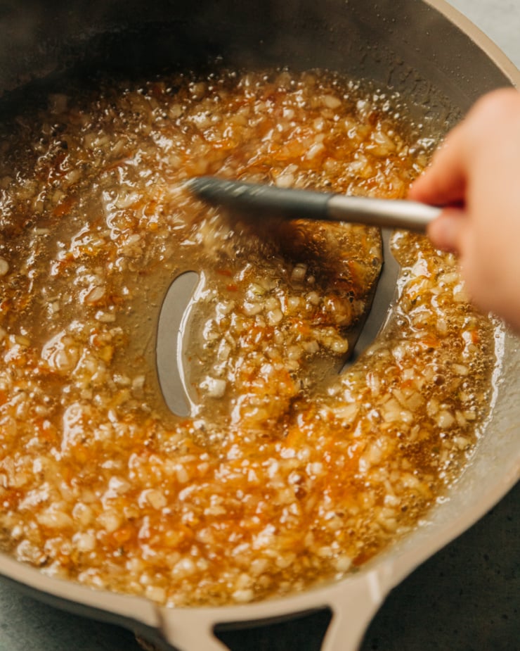 A hand is using a spatula to stir up a marmalade based glaze in a non-stick skillet.