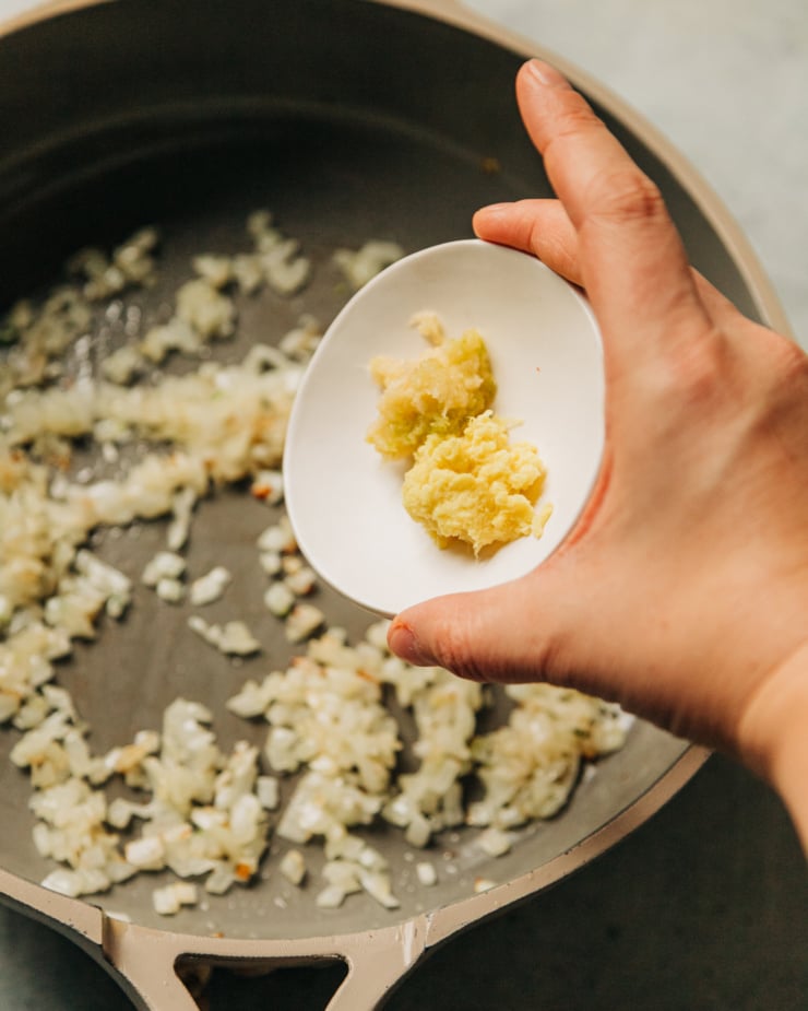 A hand is holding a small bowl with finely minced/grated ginger and garlic.