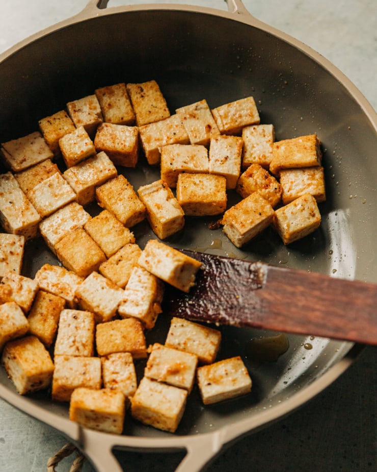 A slight 3/4 angle shot of tofu being cooked in a non-stick skillet.