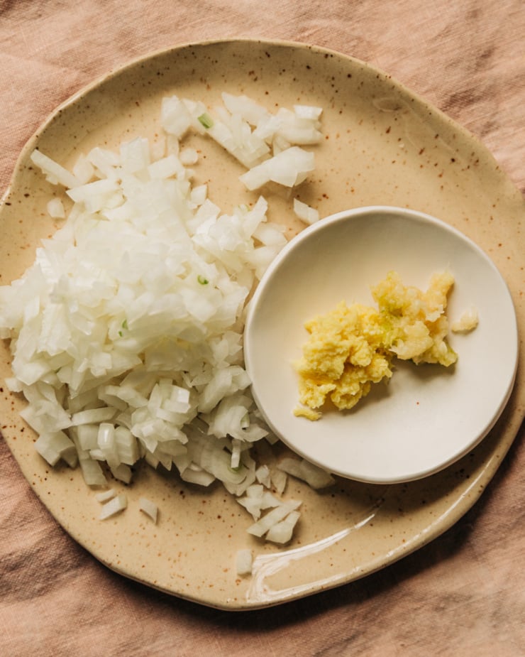 An overhead shot shows a plate with small dice onions and an even smaller bowl with finely minced ginger and garlic.