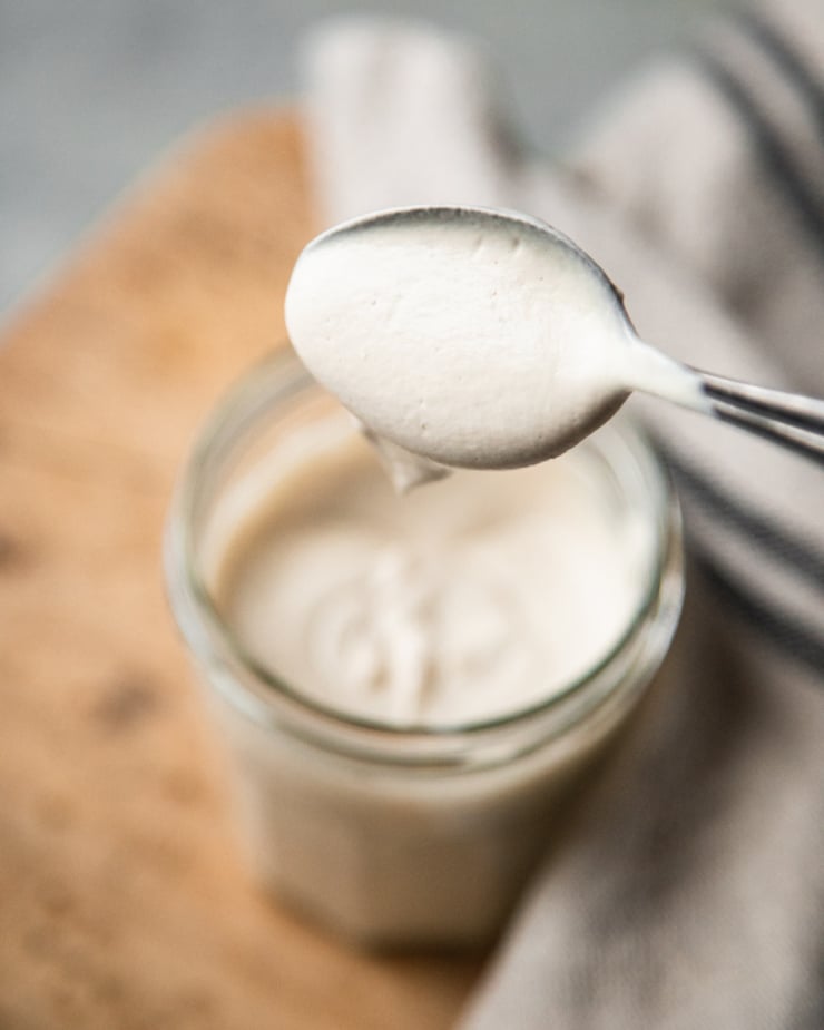 A slight 3/4 angle shot shows a spoon lifting a bit of vegan sour cream out of a glass jar.
