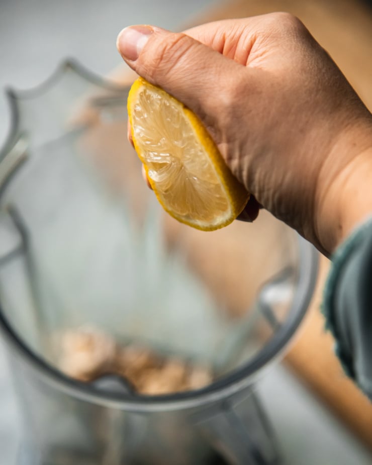 A slight 3/4 angle image shows a hand squeezing a lemon half into a blender pitcher.