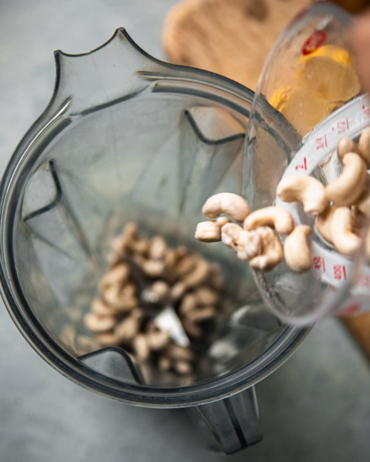 An overhead shot of cashews being poured into a blender pitcher.