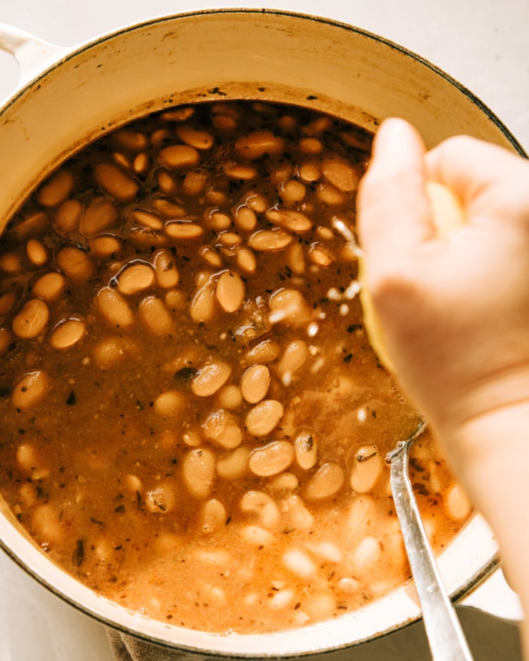 A hand is squeezing a lemon half into a pot of beans. An overhead shot.