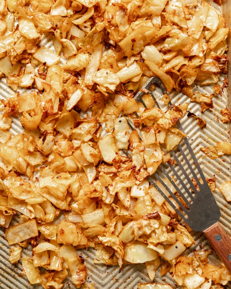 An overhead shot shows chopped cabbage that's been roasted on a sheet pan with slightly brown edges.