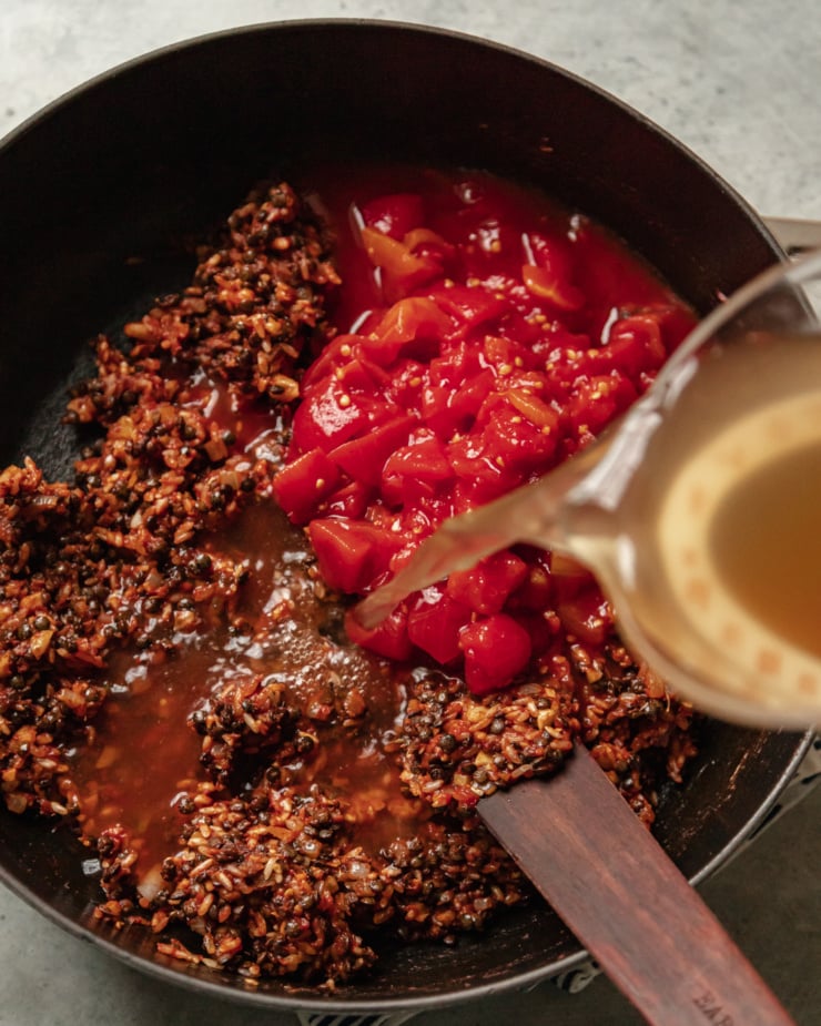 An overhead shot shows vegetable stock being poured into a pot with lentils, onions, rice, walnuts, and chopped canned tomatoes.