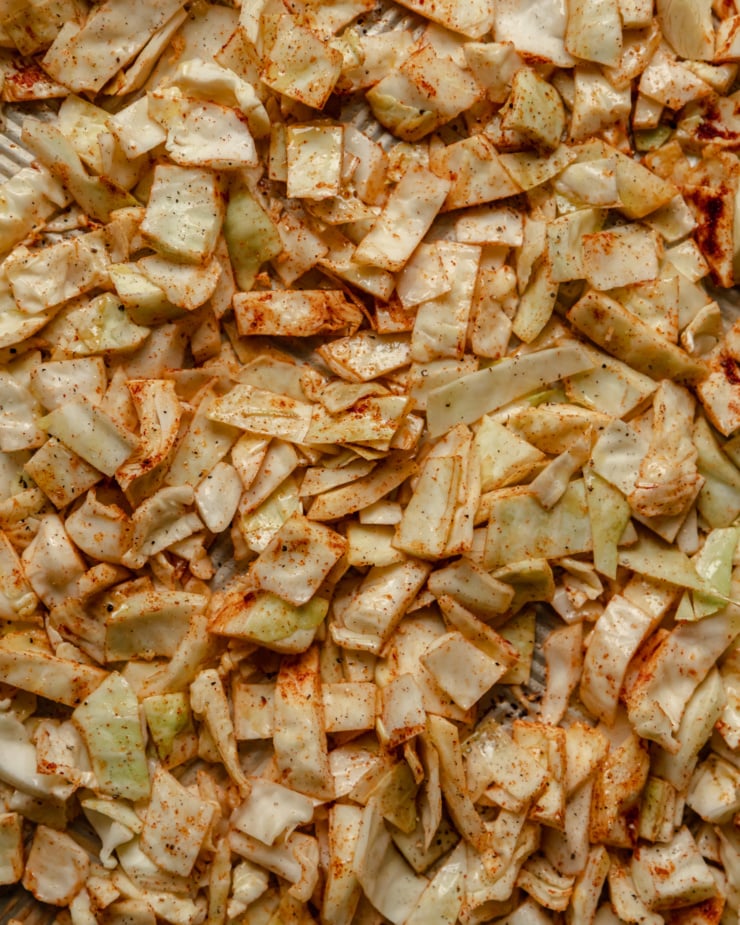 An up close, overhead shot shows chopped cabbage coated in oil and spices and spread out evenly in a single layer on a baking sheet.