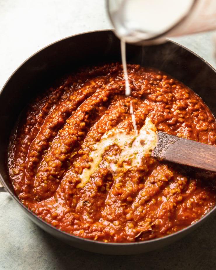 A 3/4 angle image shows non0dairy creamer being poured into a tomato-y sauce in a wide pot.