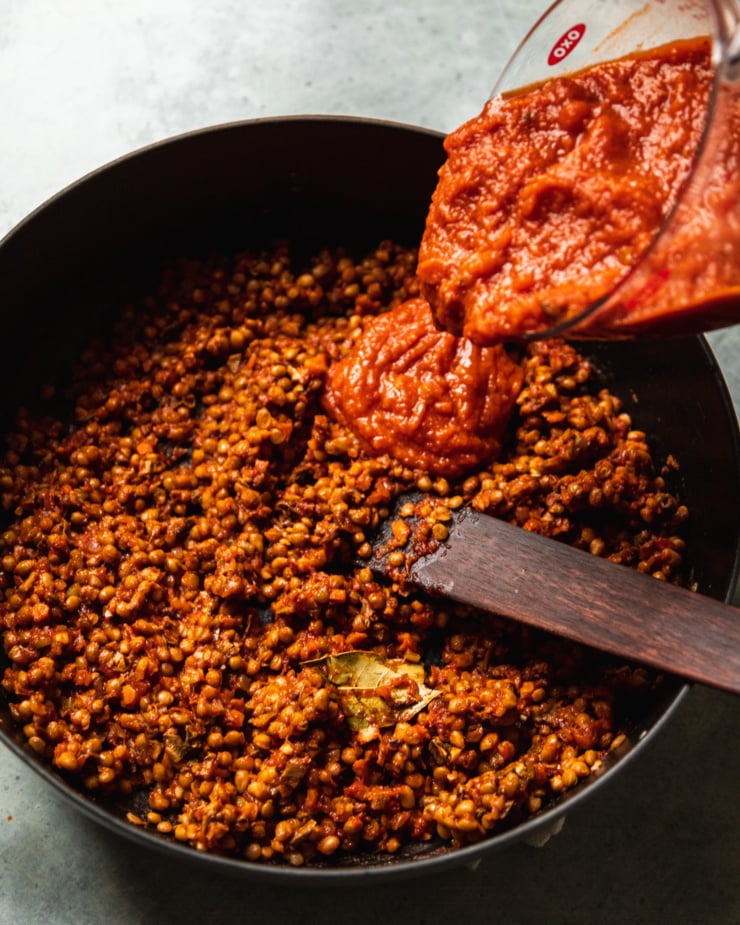 An overhead shot shows marinara sauce being poured into a pot filled with seasoned lentils.