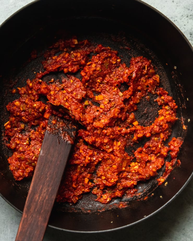 An overhead shot shows tomato paste and finely diced vegetables in a braiser pot that have been cooked down into an intensely flavourful paste.