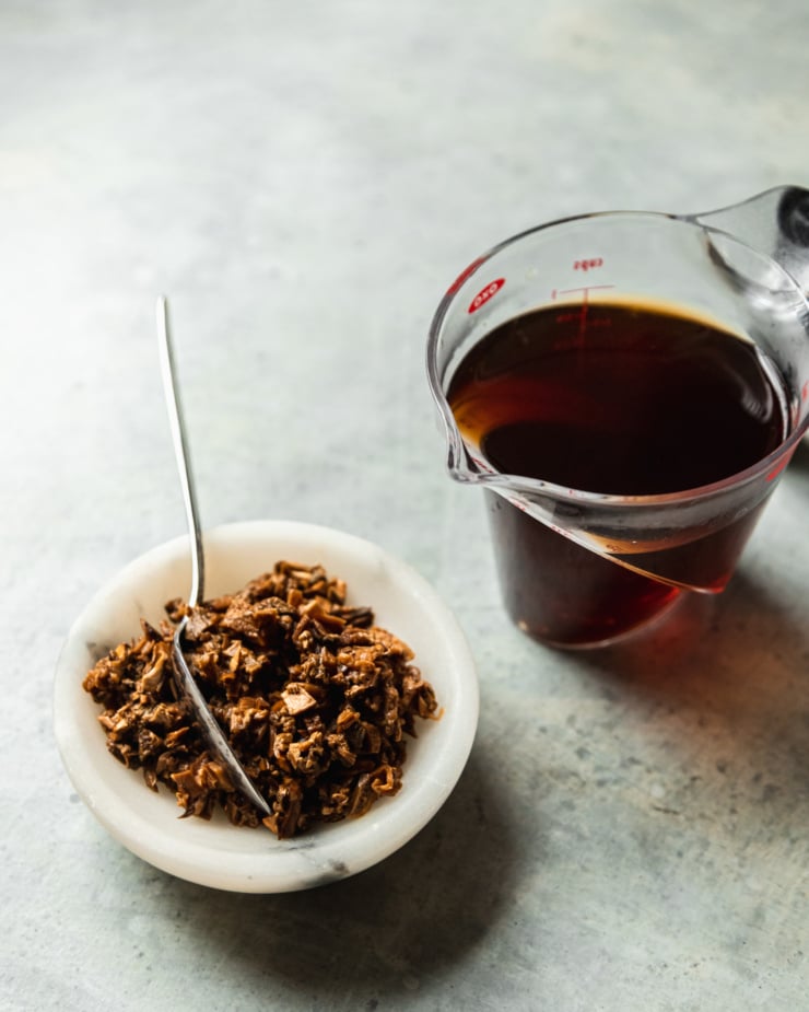 A 3/4 angle image shows re-hydrated and minced dried porcini mushrooms and a measuring cup filled with the porcini soaking liquid/