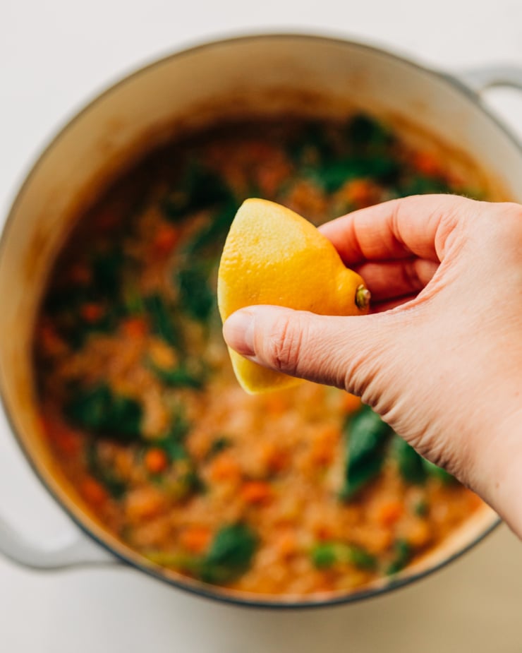 A hand is squeezing a lemon half into a pot of soup.