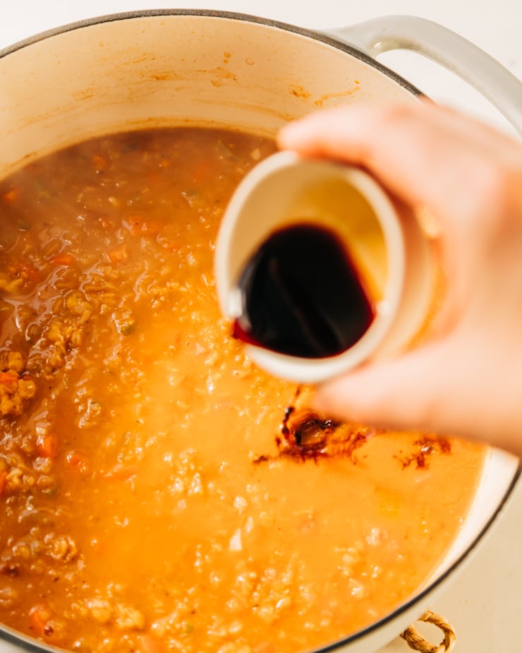 A hand is pouring some Tamari from a bowl into a pot of soup.
