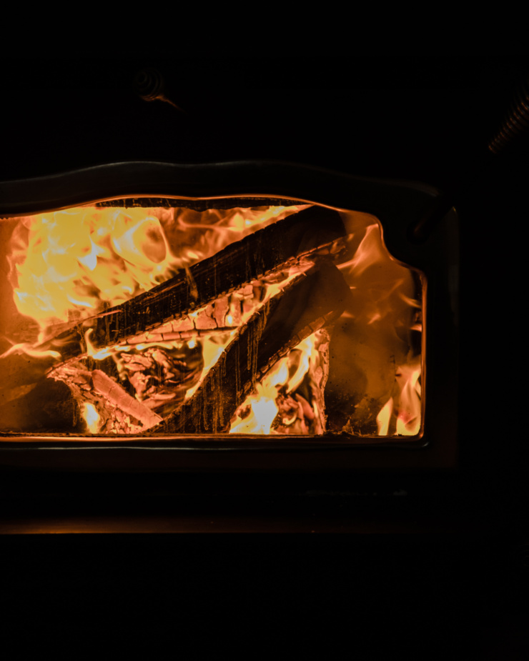 An up close, head-on shot shows wood burning in a wood stove in strong contrast.