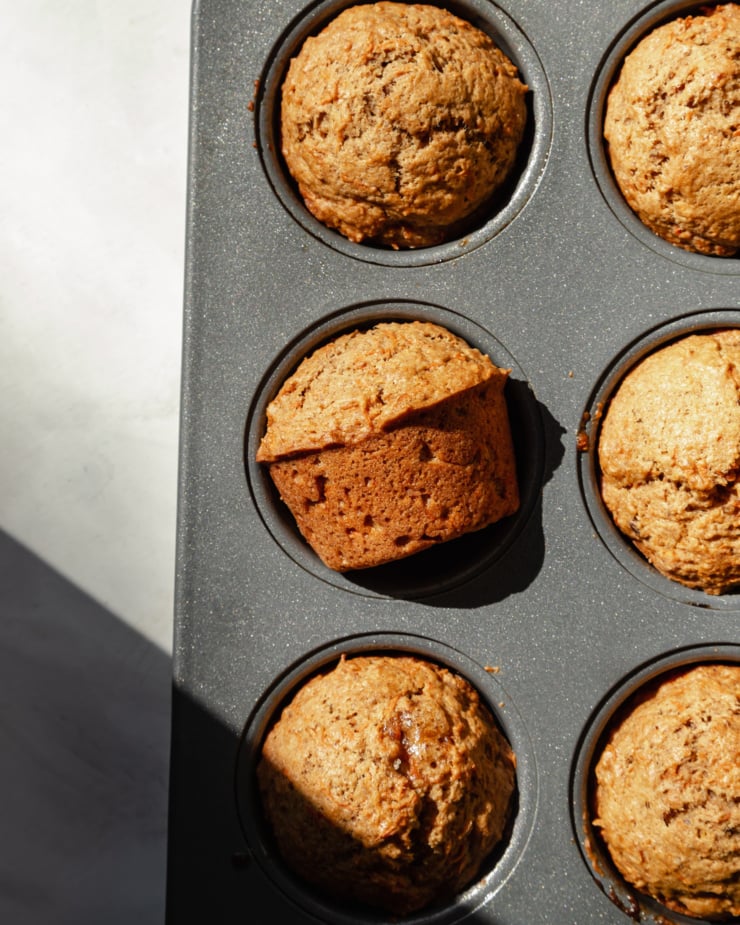 An overhead shot shows baked muffins in a muffin tin in direct sunlight.