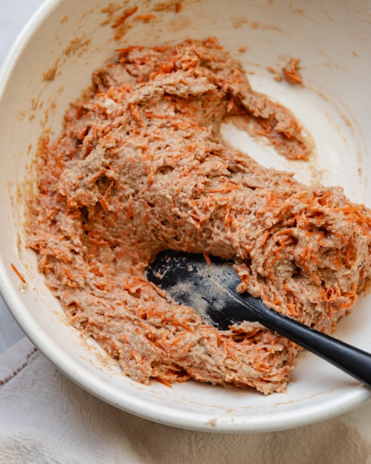 An overhead shot shows carrot muffin batter in a large mixing bowl with a spatula.