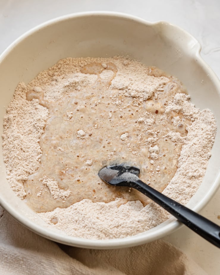 An overhead shot shows liquid ingredients being added to dry ingredients in a large mixing bowl.