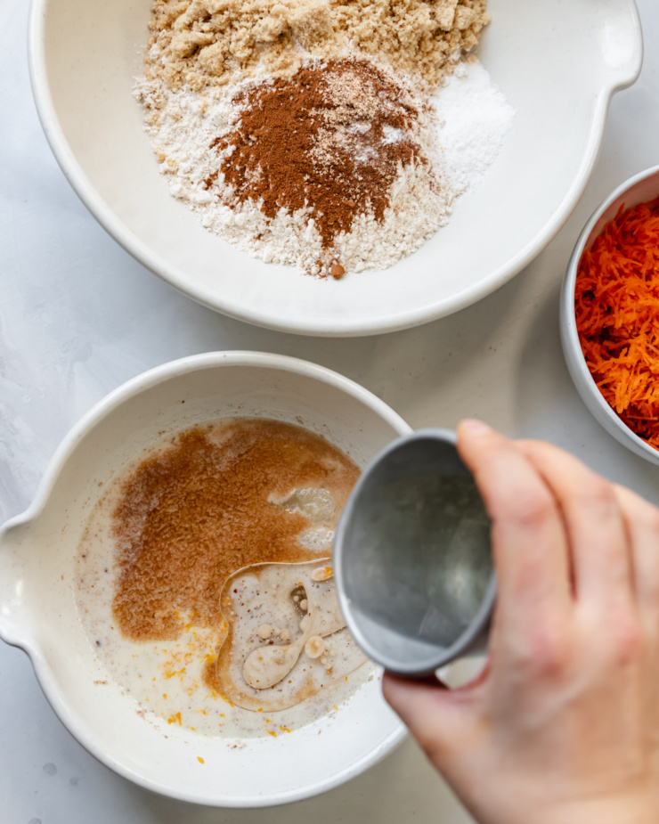 An overhead shot of 3 bowls: 1 with dry ingredients, one with wet ingredients, and one with shredded carrots. All will be combined for a muffin batter.