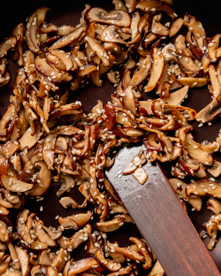An up close, overhead shot shows sliced sautéed mushrooms coated in sesame seeds.