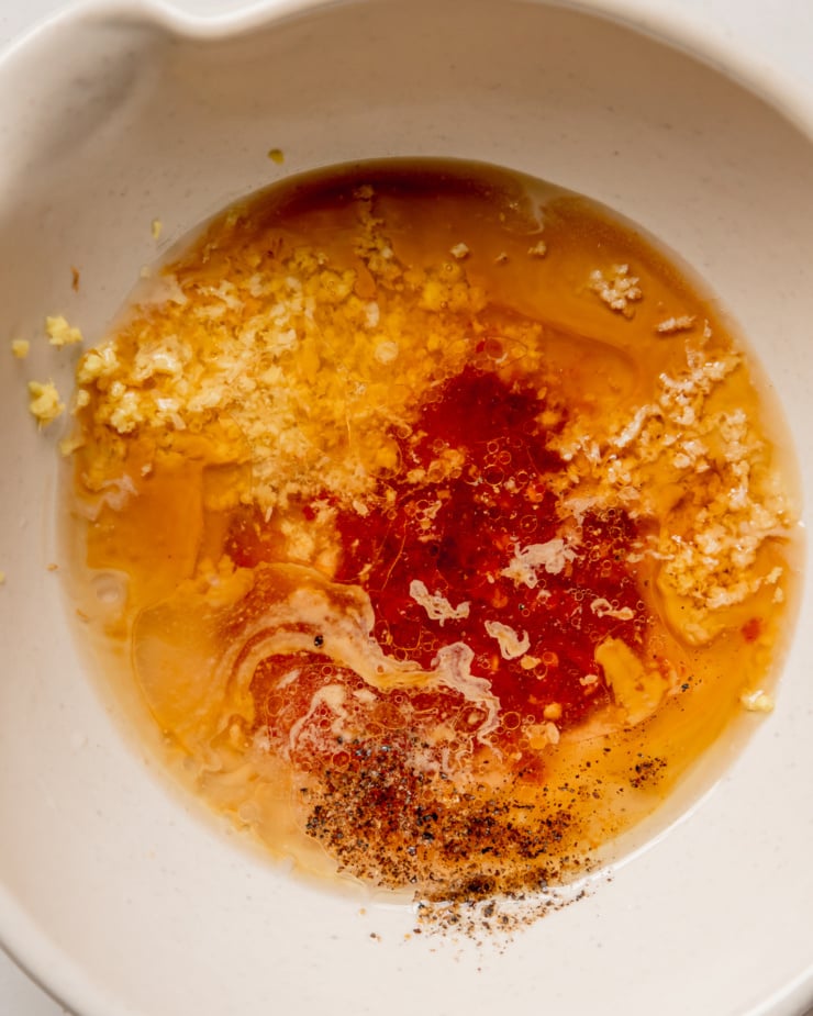An up close, overhead shot of ingredients in a small mixing bowl for a spicy sesame dressing, prior to mixing.