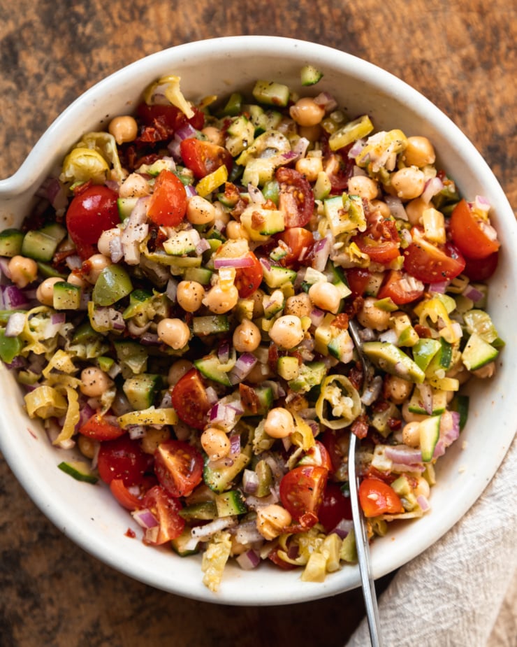 An up close, overhead shot of a chickpea, tomato, cucumber, red onion, sun dried tomato, olive, and pepperoncini mixture tossed lightly with vinaigrette.