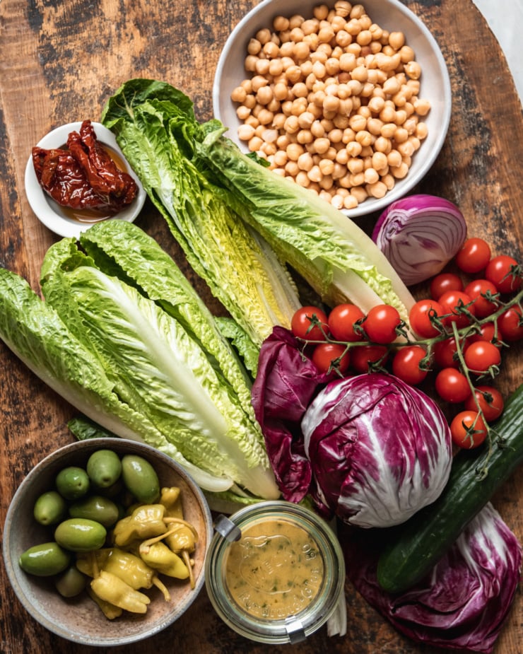 An overhead shot of ingredients used in a vegan pizza night salad, all on a worn wood surface.