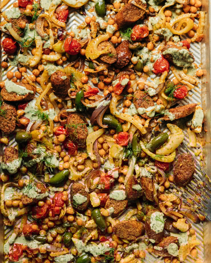 An up close, overhead shot of a veggie sausage sheet pan dinner with drizzles of pesto cream sauce on top.
