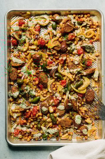 An overhead shot of a veggie sausage sheet pan dinner with pesto cream sauce drizzled on top.