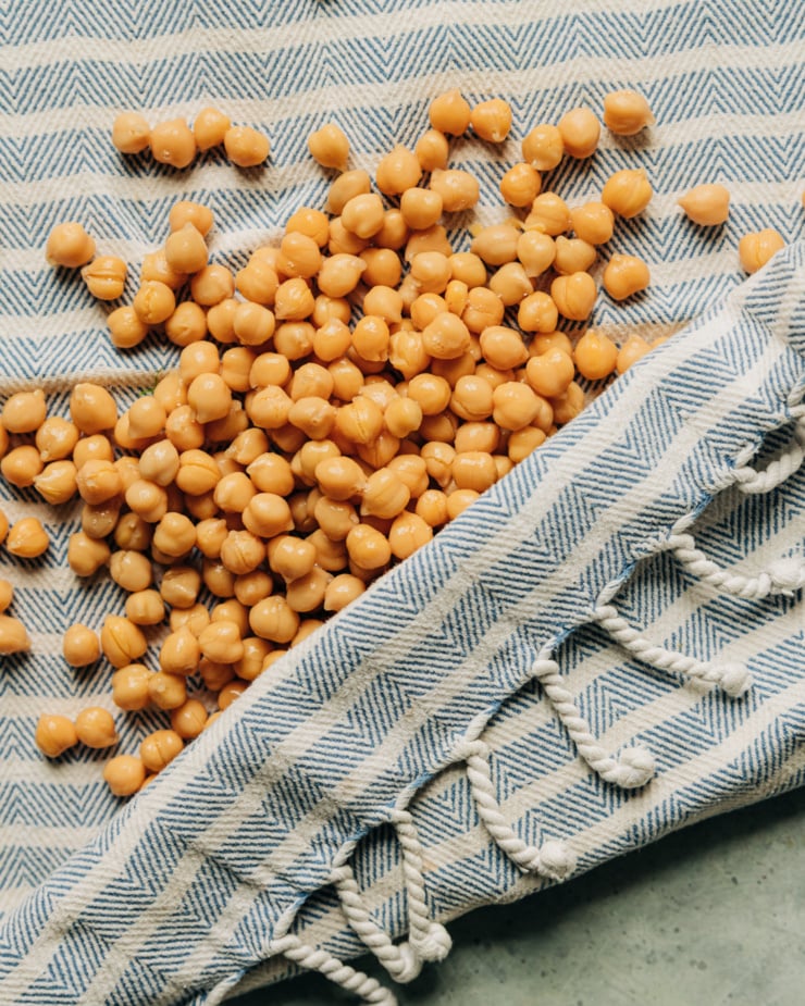 An up close, overhead shot shows chickpeas being blotted dry with a clean kitchen towel, before being roasted.
