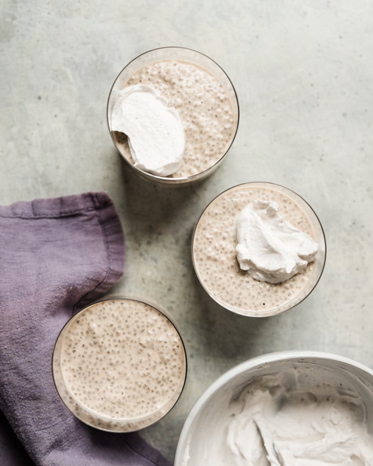 An overhead shot shows three servings of earl grey latte chia pudding in clear glasses. Two of the servings are topped with a fluffy coconut milk yogurt.