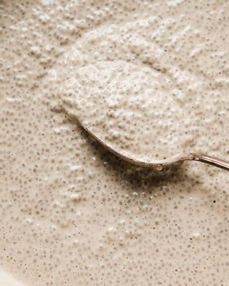 An up close overhead shot shows a batch of earl grey latte chia pudding with a spoon swooping through it. The pudding is off white and very creamy.