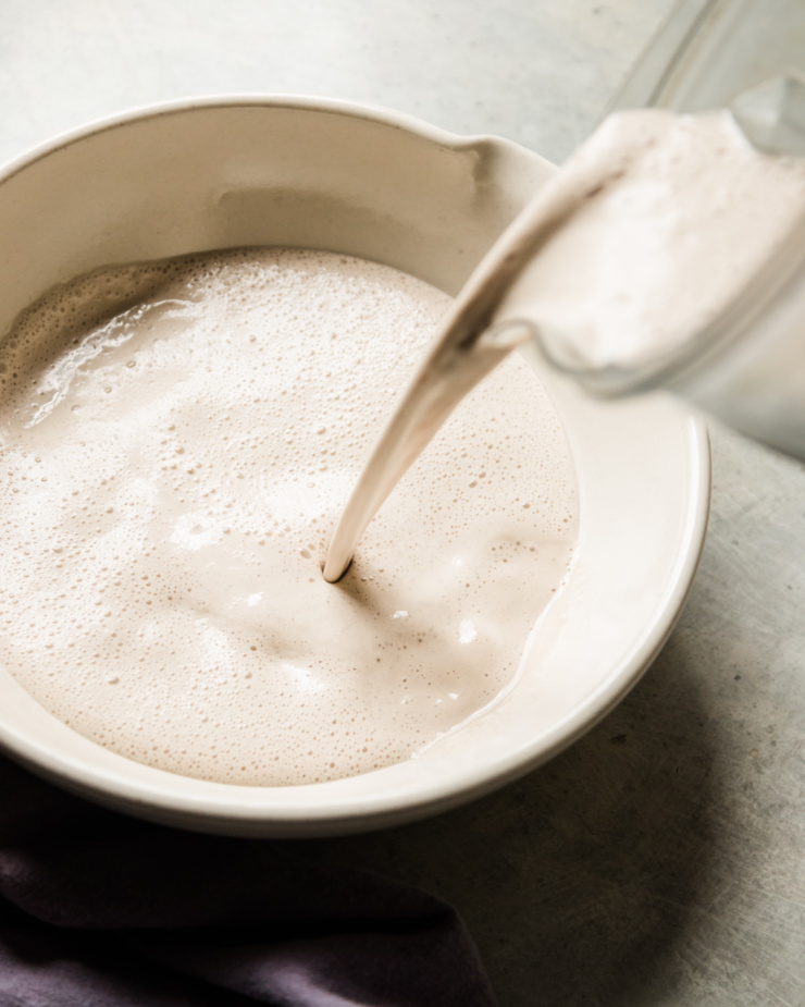 A 3/4 angle shot shows earl grey tea-infused cashew milk being poured from a blender pitcher into a large mixing bowl.