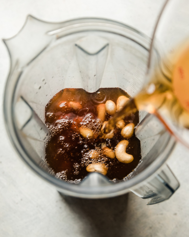 An overhead shot shows brewed earl grey tea being poured into a blender pitcher with soaked raw cashews, vanilla bean paste, and maple syrup.