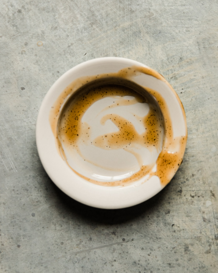 An overhead image shows a small bowl that held vanilla bean paste, but has been scraped out. Tiny vanilla seeds are seen.