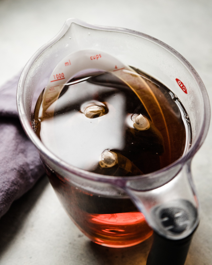 A 3/4 angle shows a large batch of earl grey tea steeping in a liquid measuring cup.