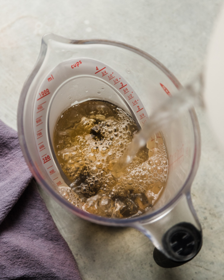 An overhead image shows hot water being added to earl grey tea bags in a large measuring cup.